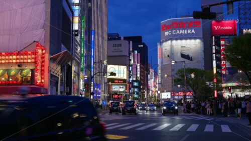 Tokyo, Japan – April 12, 2025: View of the vibrant life of Shinjuku City with people and cars moving on the streets with lighted buildings in the evening. Translation: “Advertiser recruitment” - Starpik Stock