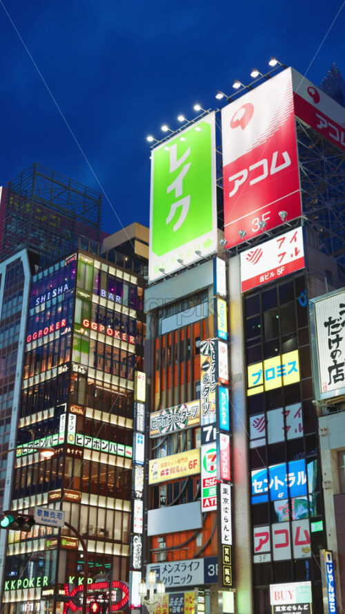 Tokyo, Japan – April 12, 2025: View of the vibrant life of Shinjuku City with people and cars moving on the streets with lighted buildings in the evening. Translation: “Kabukicho impact”. Vertical - Starpik Stock