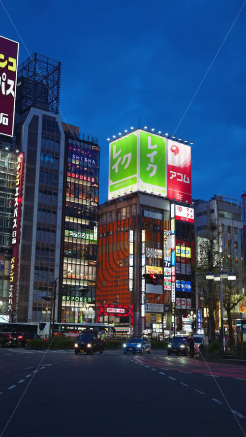 Tokyo, Japan – April 12, 2025: View of the vibrant life of Shinjuku City with people and cars moving on the streets with lighted buildings in the evening. Translation: “Kabukicho impact”. Vertical - Starpik Stock