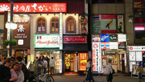 Tokyo, Japan – April 12, 2025: View of the vibrant life of Shinjuku City with people moving on the streets with lighted buildings in the evening. Translation: “Company names” - Starpik Stock