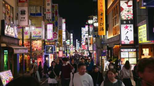 Tokyo, Japan – April 12, 2025: View of the vibrant life of Shinjuku City with people moving on the streets with lighted buildings in the evening. Translation: “Company names” - Starpik Stock