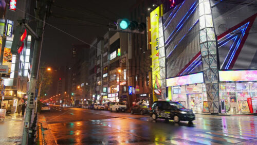 Tokyo, Japan – April 13, 2025: People and cars moving on the streets of the city with orange lights on a rainy evening - Starpik Stock