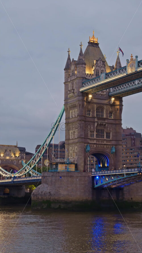 Tower Bridge close-up with some people walking on the bridge and its iconic towers lit up in blue in London, England. Vertical - Starpik Stock