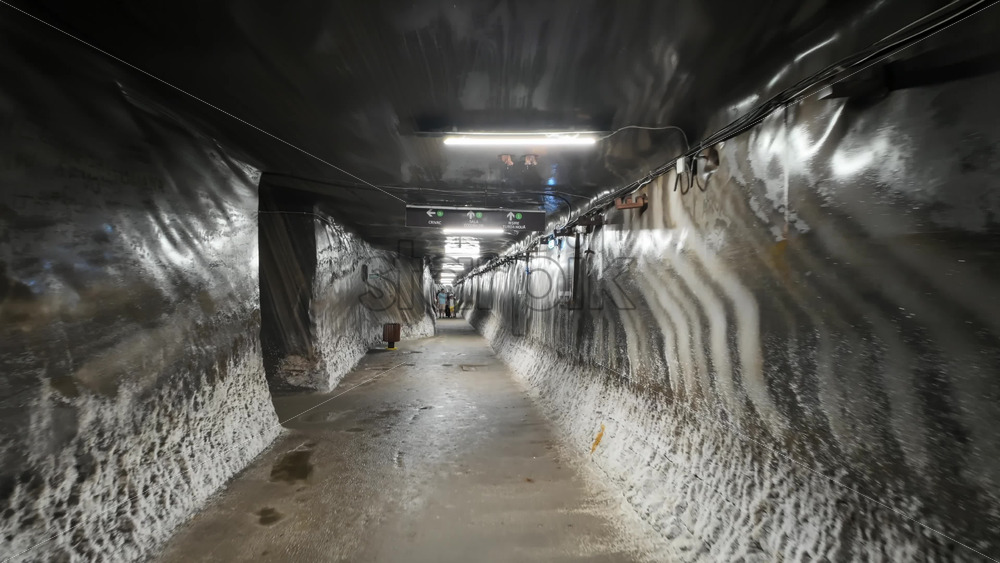 Turda, Romania – July 20, 2025: A narrow, illuminated tunnel inside the Turda Salt Mine with directional signage for visitors. Translation: “Direction signs and location names” - Starpik Stock