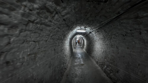 Turda, Romania – July 20, 2025: Narrow tunnel with dim lighting and visitors walking inside at the Turda Salt Mine - Starpik Stock