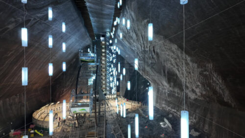 Turda, Romania – July 20, 2025: View of people walking through the underground amusement park inside the Turda salt mine, with rides, a Ferris wheel, and glowing blue lights suspended from the ceiling - Starpik Stock