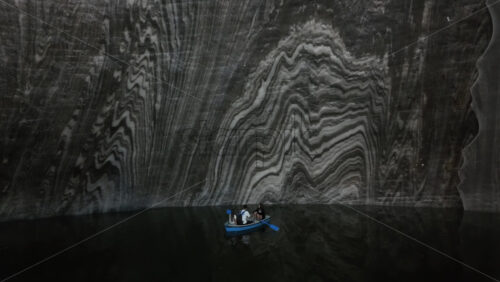 Turda, Romania – July 20, 2025: Visitors rowing small boats on a dark underground salt lake surrounded by wooden platforms and illuminated cavern walls at the Turda Salt Mine - Starpik Stock