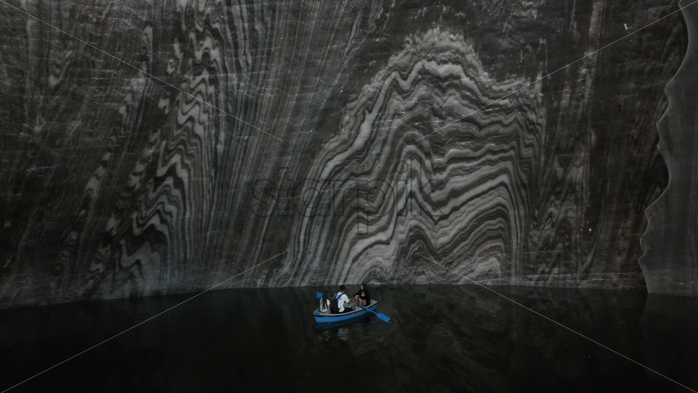 Turda, Romania – July 20, 2025: Visitors rowing small boats on a dark underground salt lake surrounded by wooden platforms and illuminated cavern walls at the Turda Salt Mine - Starpik Stock