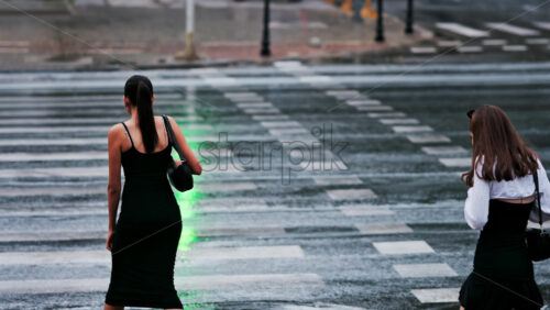 Two girls crossing the street at a green light on a rainy day in Chisinau, Moldova - Starpik Stock