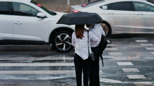 Two girls holding an umbrella waiting at a pedestrian crossing on a rainy day in Chisinau, Moldova - Starpik Stock