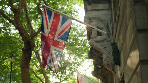 Union Jack flag hanging on a historic building with green trees on the background in London, England - Starpik Stock