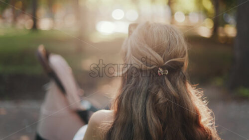 Video – A mother with long wavy hair siting on a bench, breastfeeding her baby in a peaceful park, next to a modern baby stroller - Starpik Stock