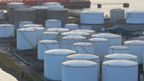 Video – Aerial drone view of large oil storage tanks in Copenhagen Harbor, Denmark, with offshore wind turbines and the sea in the background at sunset - Starpik Stock