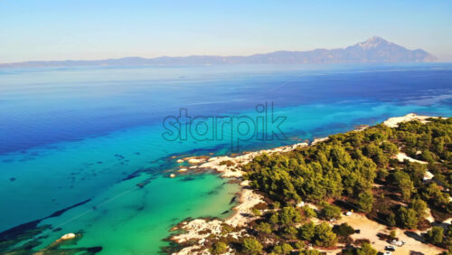 Video – Aerial drone view of the Aegean sea rocky coast with blue transparent water, multiple greenery, mountain on the background. Greece - Starpik Stock