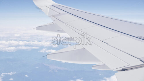 Video – Bright window seat view of an airliner wing cruising above a sea of clouds under a clear blue sky - Starpik Stock