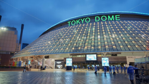 Video - Bunkyo, Japan - April 13, 2025: The entrance of the Tokyo Dome Stadium with staff walking around on a rainy evening
