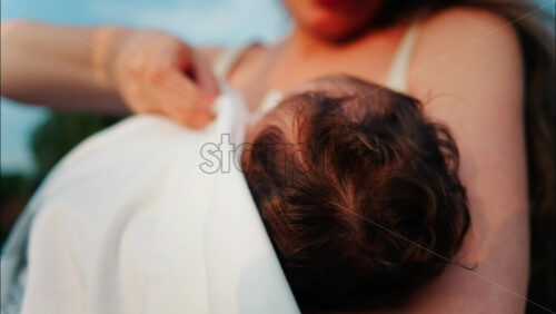 Video – Close up of a mother holding her newborn in her arms outdoors during sunset - Starpik Stock