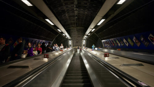 Video – London, England – May 12, 2025: Wide-angle view of a deep London Underground escalator tunnel with people ascending and descending in the evening - Starpik Stock
