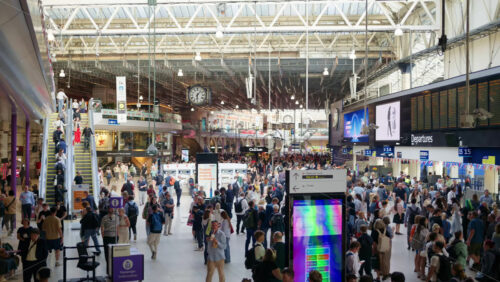 Video – London, England – May 14, 2025: Commuters walking beneath the iconic departure board in the sunlit interior of Waterloo Station - Starpik Stock