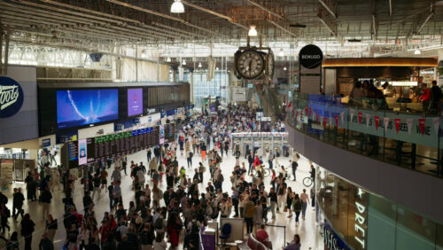 Video – London, England – May 14, 2025: Commuters walking beneath the iconic departure board in the sunlit interior of Waterloo Station - Starpik Stock