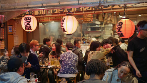 Video - Shinjuku, Japan - April 12, 2025: Chef cooking and people sitting at a traditional Japanese restaurant on the Omoide Yokocho Memory Lane in the evening. Translation: "Shibuya"