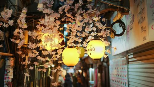 Video – Shinjuku, Japan – April 12, 2025: Lighted paper lanterns hanging with cherry blossom flower decorations on the on the Omoide Yokocho Memory Lane in the evening. Translation: “Restaurant name” - Starpik Stock