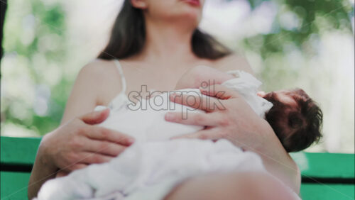 Video – Tender moment of a mother breastfeeding her baby on a green park bench in daylight - Starpik Stock