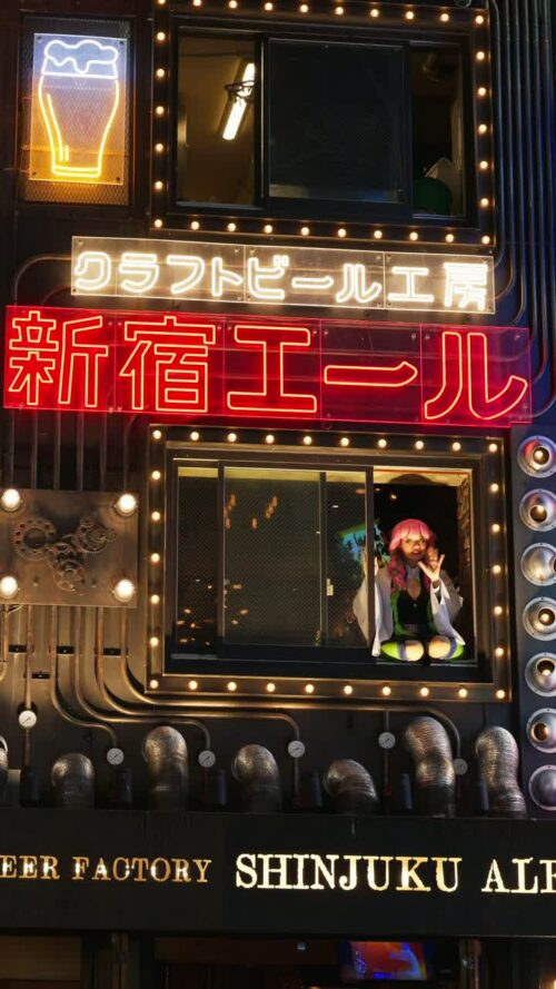 Video – Tokyo, Japan – April 12, 2025: Girl with pink hair waving from the window of the Craft Beer Factory Shinjuku Ale in the evening. Translation: “Craft Beer Factory Shinjuku Ale”. Vertical - Starpik Stock