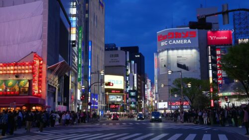 Video – Tokyo, Japan – April 12, 2025: View of the vibrant life of Shinjuku City with people and cars moving on the streets with lighted buildings in the evening. Translation: “Advertiser recruitment” - Starpik Stock