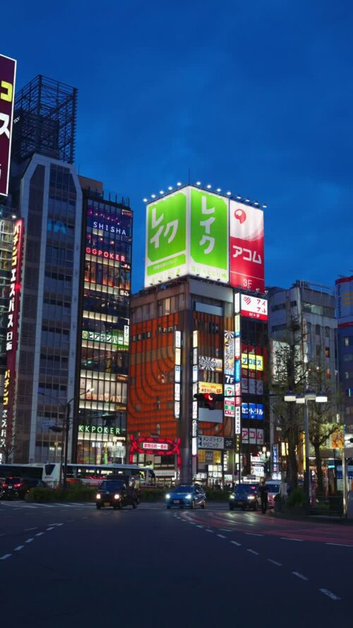 Video – Tokyo, Japan – April 12, 2025: View of the vibrant life of Shinjuku City with people and cars moving on the streets with lighted buildings in the evening. Translation: “Kabukicho impact”. Vertical - Starpik Stock