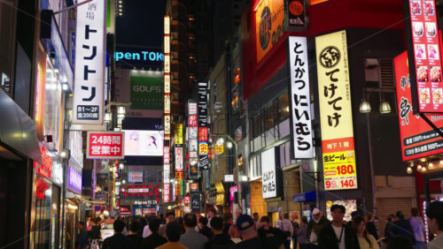 Video - Tokyo, Japan - April 12, 2025: View of the vibrant life of Shinjuku City with people moving on the streets with lighted buildings in the evening. Translation: "Company names"