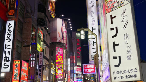 Video - Tokyo, Japan - April 12, 2025: View of the vibrant life of Shinjuku City with people moving on the streets with lighted buildings in the evening. Translation: "Company names"