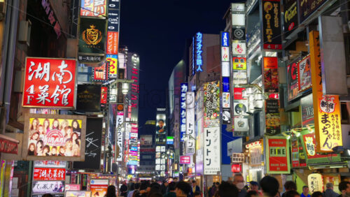 Video - Tokyo, Japan - April 12, 2025: View of the vibrant life of Shinjuku City with people moving on the streets with lighted buildings in the evening. Translation: "Company names"