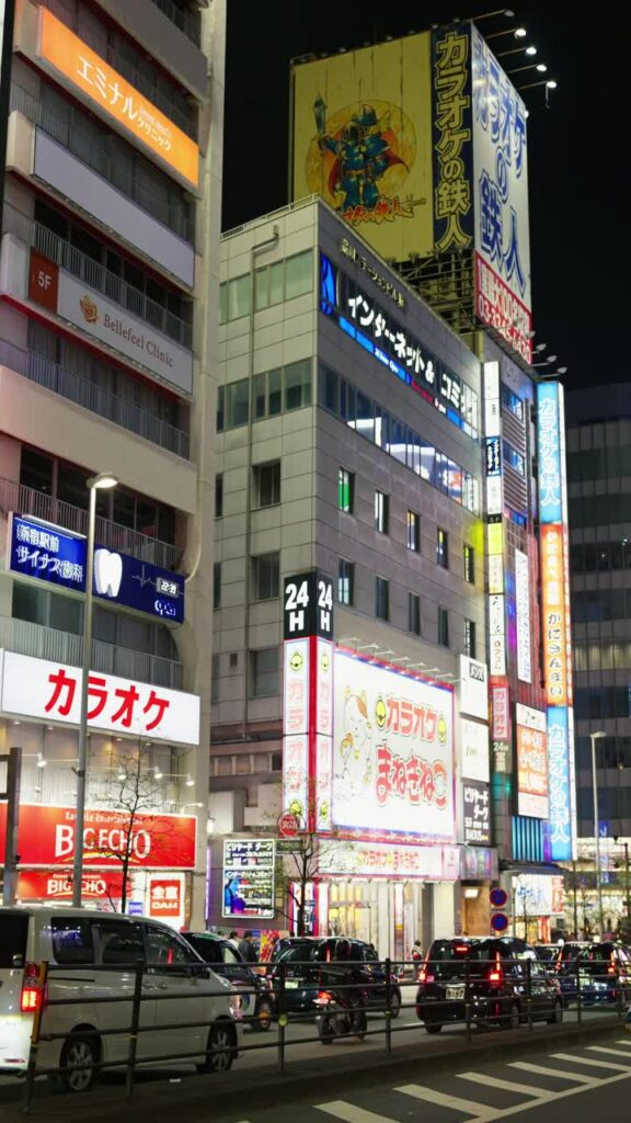 Video – Tokyo, Japan – April 12, 2025: View of the vibrant life of Shinjuku City with people moving on the streets with lighted buildings in the evening. Translation: “Company names”. Vertical - Starpik Stock