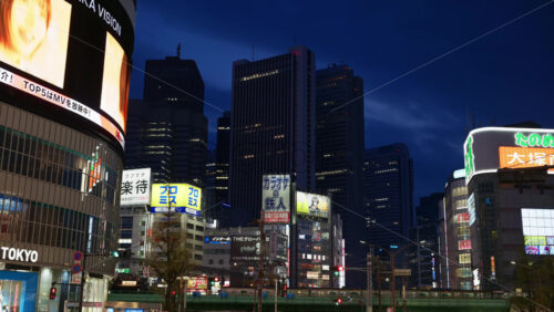 Video - Tokyo, Japan - April 12, 2025: View of the vibrant life of Shinjuku City with train moving on the streets with lighted buildings in the evening. Translation: "Company names"