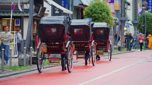 Video - Tokyo, Japan - April 13, 2025: Multiple tourists riding in rickshaws near the Senso-ji temple in Asakusa. Translation: "Company name"