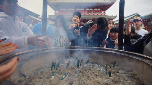 Video - Tokyo, Japan - April 13, 2025: People burning incense on a jokoro at the Senso-ji temple in daylight