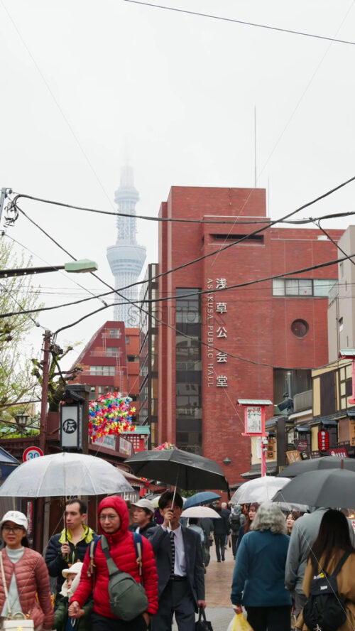 Video - Tokyo, Japan - April 13. 2025: Distat view of the Tokyo Skytree surrounded by clouds with people walking on a rainy day. Vertical