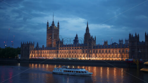 Video – View of the Palace of Westminster at night with its lights reflecting on the River Thames and a sightseeing boat passing by, London, England - Starpik Stock