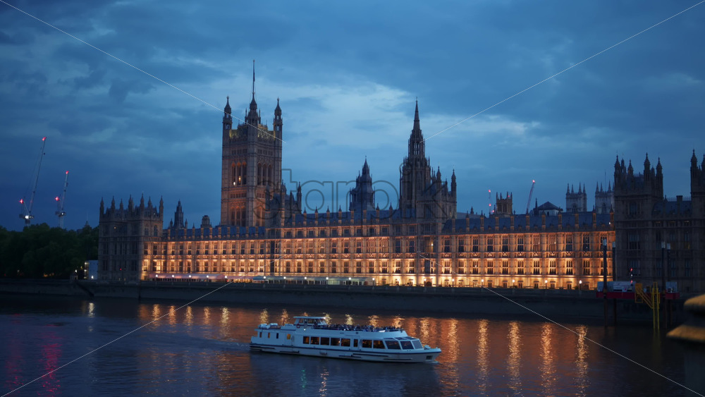 Video – View of the Palace of Westminster at night with its lights reflecting on the River Thames and a sightseeing boat passing by, London, England - Starpik Stock