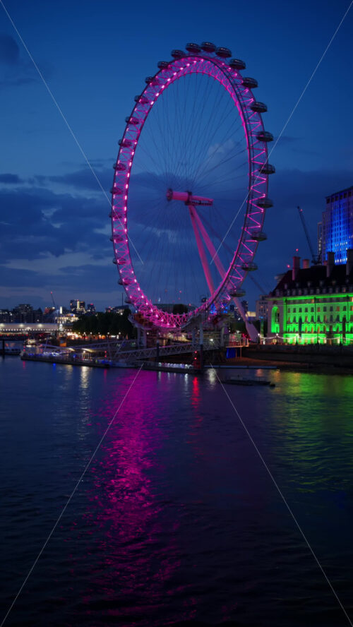 View of London Eye glowing pink and County Hall lit in green in the evening. Vertical, London - Starpik Stock