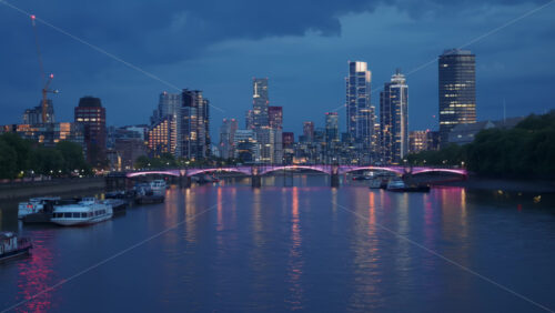 View of River Thames with city lights reflecting on the water and boats docked along the shore in the evening in London, England - Starpik Stock