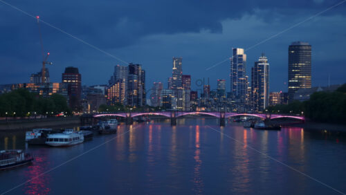 View of River Thames with city lights reflecting on the water and boats docked along the shore in the evening in London, England - Starpik Stock
