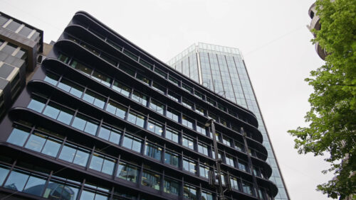 View of a sleek modern office building with large glass windows reflecting the city, surrounded by trees in London, England - Starpik Stock