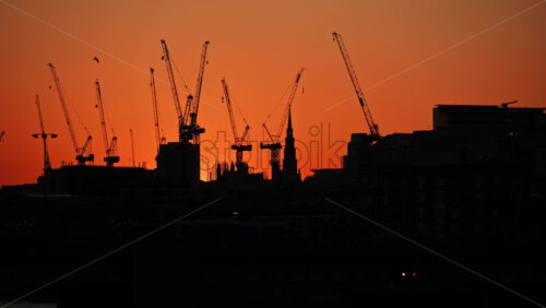 View of a vibrant sunset over silhouettes of cranes and the skyline of London, England - Starpik Stock