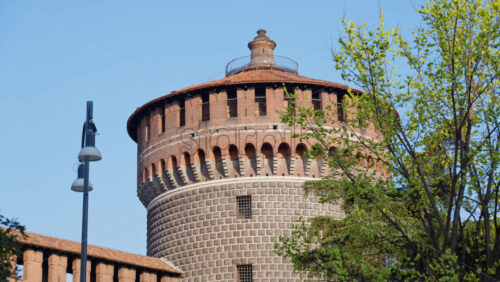 View of the Sforzesco Castle in Milan, Italy, surrounded by green trees on a blue sky background - Starpik Stock