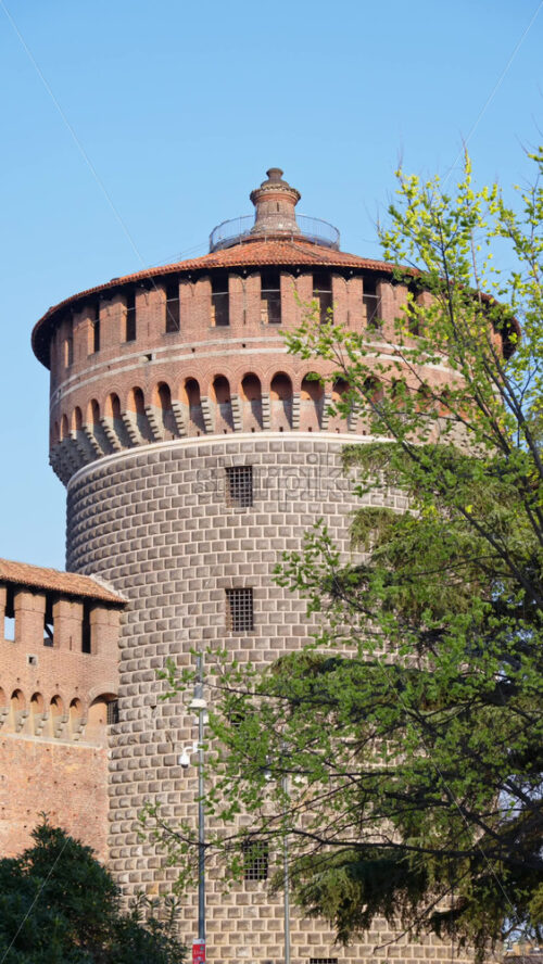 View of the Sforzesco Castle in Milan, Italy, surrounded by green trees on a blue sky background. Vertical - Starpik Stock