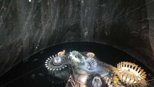 View of the underground Turda salt mine lake with illuminated wooden platforms and modern installations, surrounded by boats - Starpik Stock