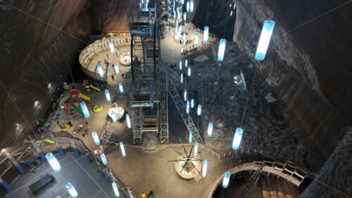 View of the underground amusement park inside the Turda salt mine, with rides, a Ferris wheel, and glowing blue lights suspended from the ceiling in Romania - Starpik Stock