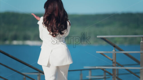 Woman in a white suit walking on a scenic terrace with a view of a calm body of water - Starpik Stock